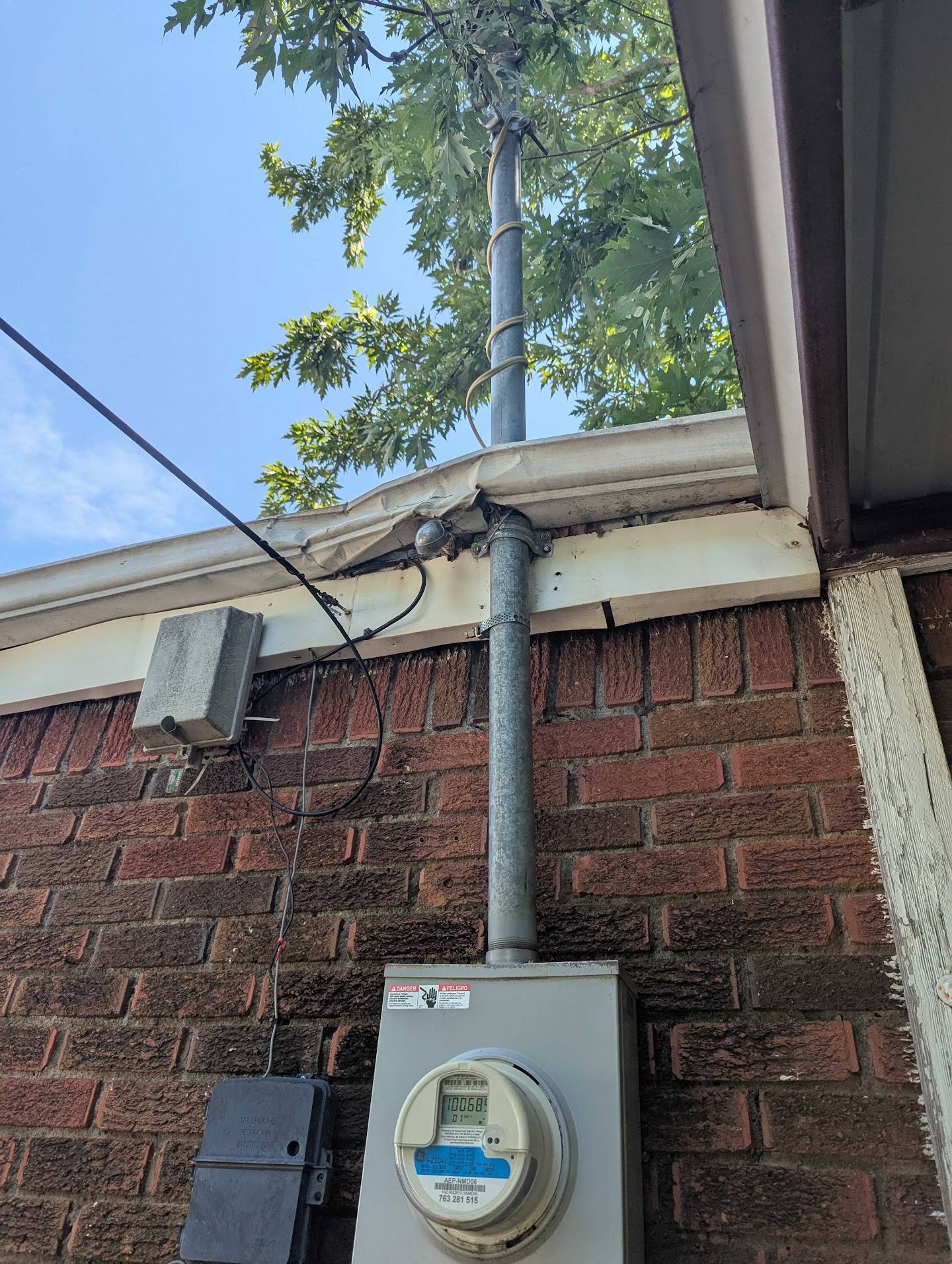 Electrical service mast pulling against a damaged gutter and fascia on a brick home