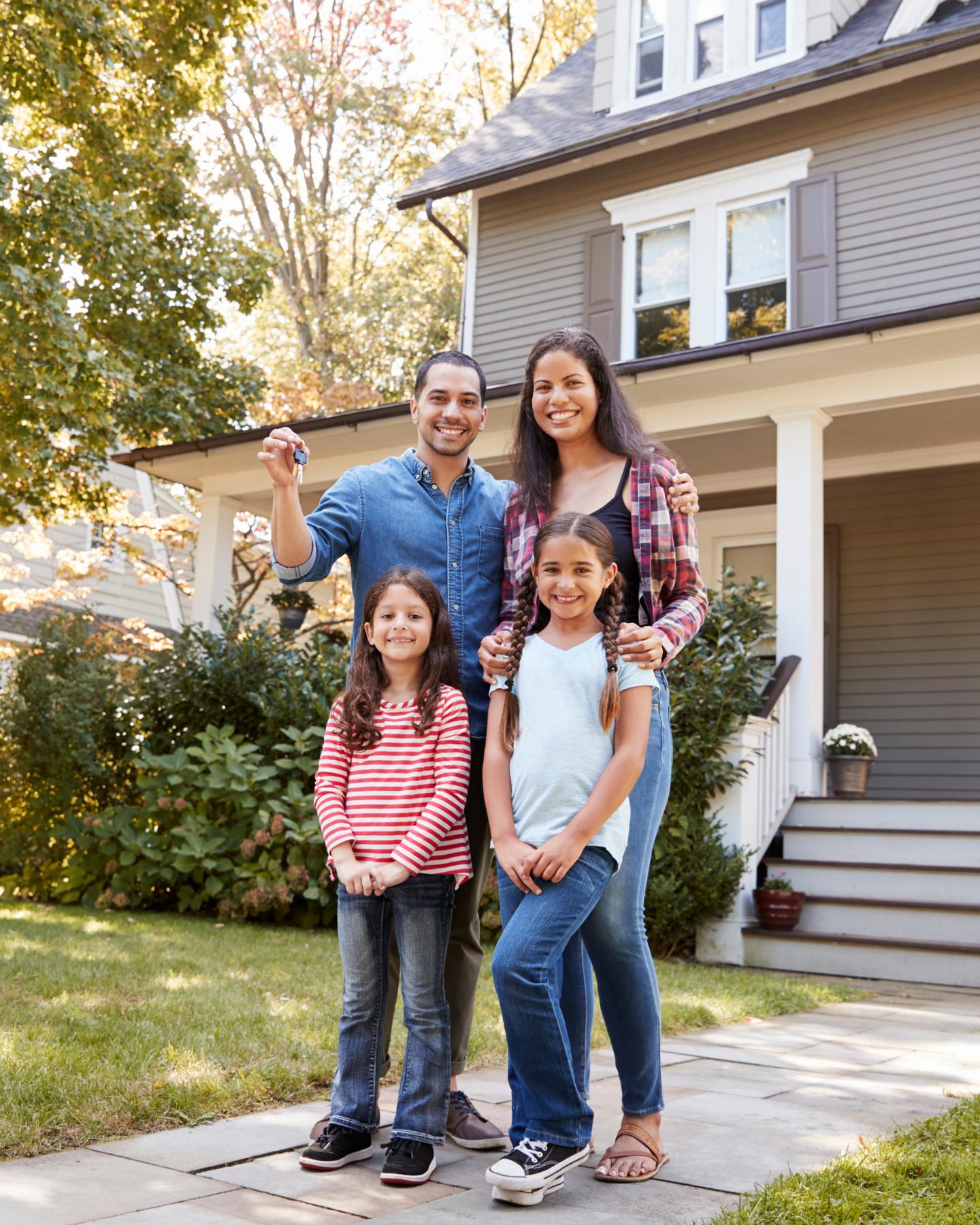 Family holding the keys to their new home in front of the house