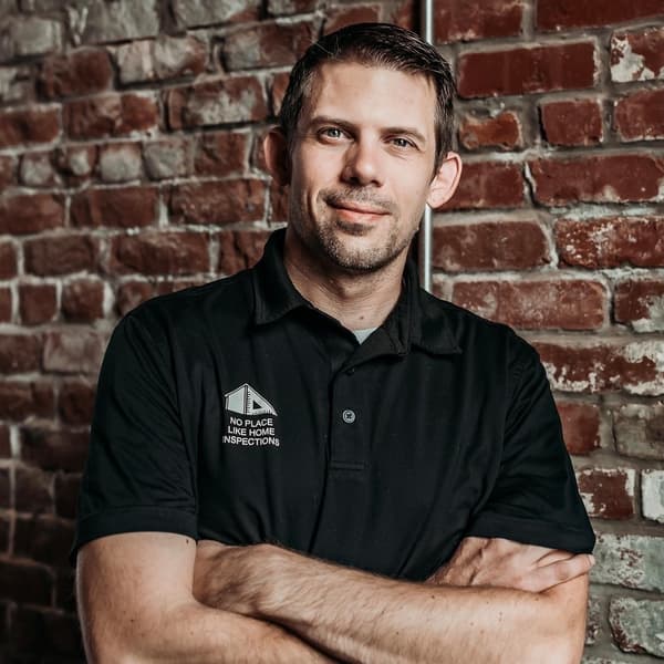 Wade Svetgoff, inspector, in a black company polo with arms crossed in front of a brick wall
